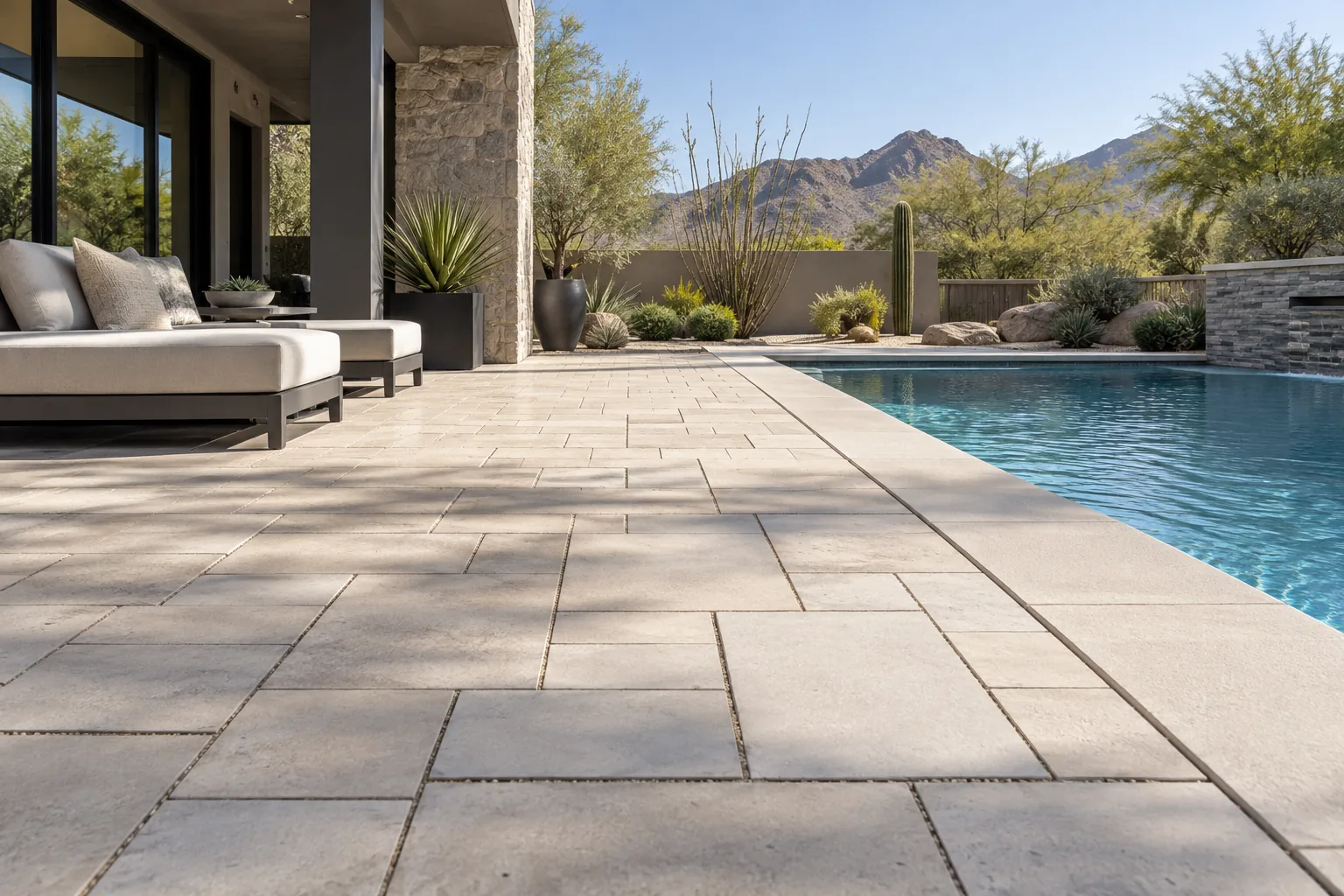 Light-colored paver pool patio with shaded seating and desert landscaping in Arizona
