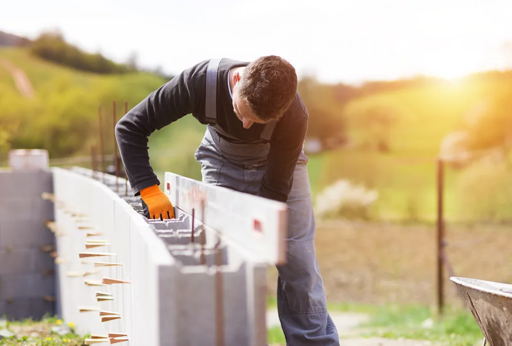 Hardscape installer leveling a row of concrete blocks for an outdoor wall